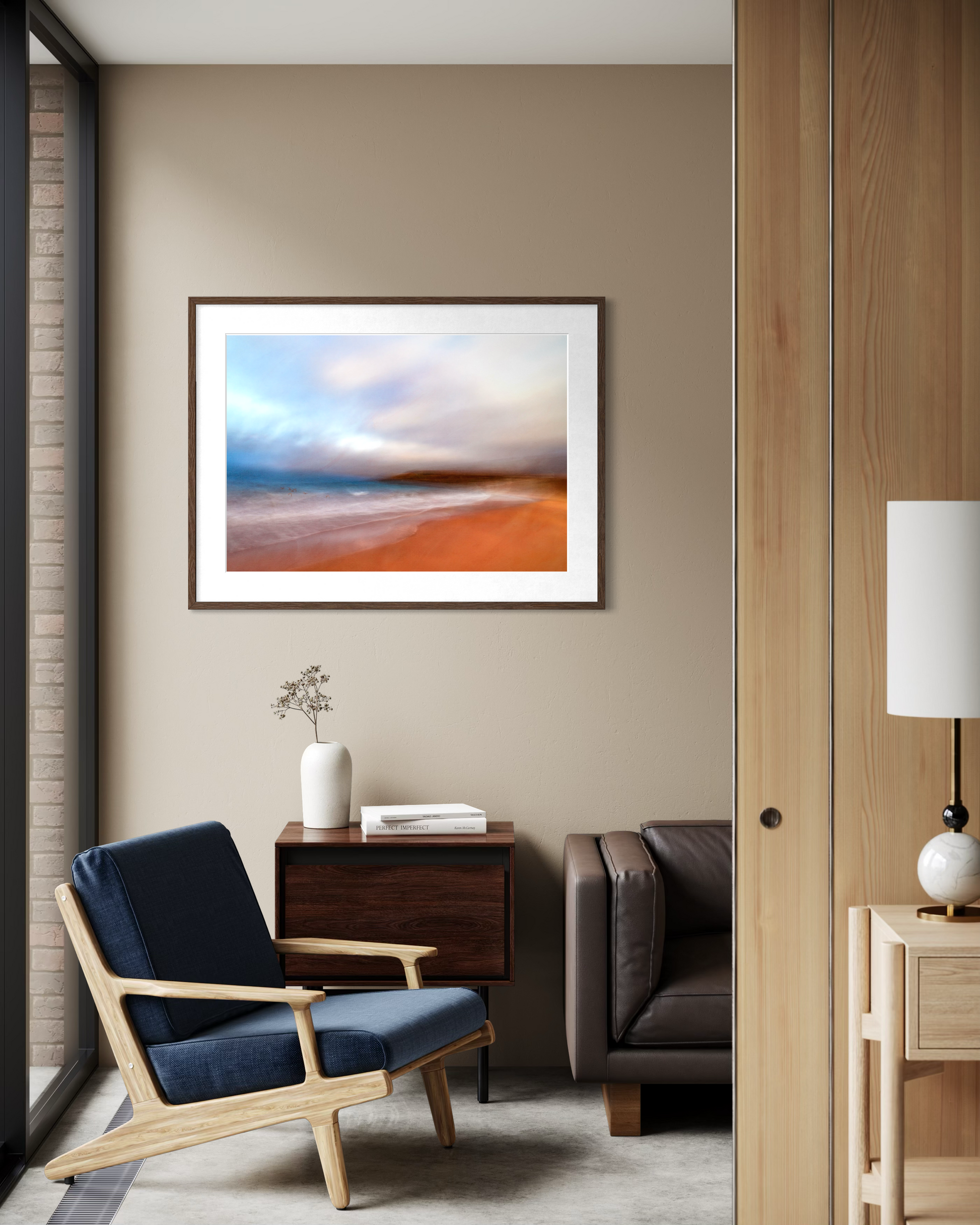 Modern living room with a blue armchair, sofa, and framed beach scene on the wall.