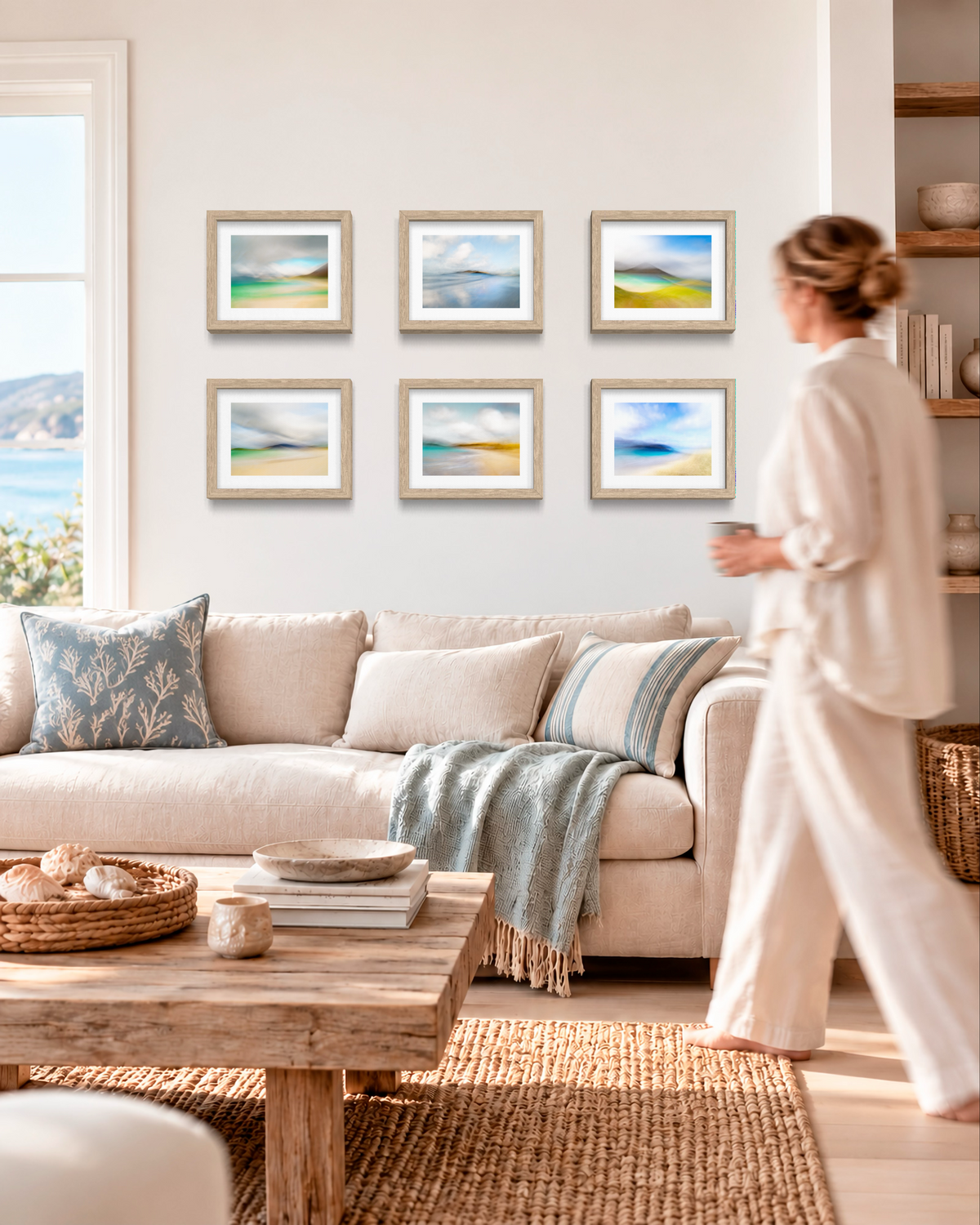 A woman in a cream lounge set walks past a beige sofa in a bright living room. Above the sofa, six framed square landscape prints with light wood frames are arranged in two rows on a white wall.